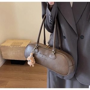 Close-up of a taupe cylinder Boston shoulder bag with a plush monster pendant
