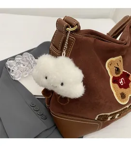Close-up of brown suede bucket tote bag with cartoon bear embroidery and plush charm