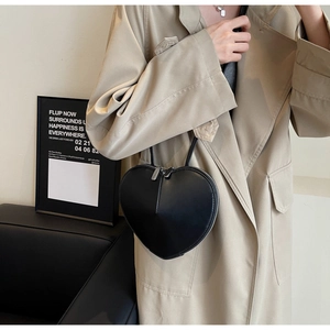 Vista dettagliata di una borsa a tracolla nera a forma di cuore indossata con un trench beige