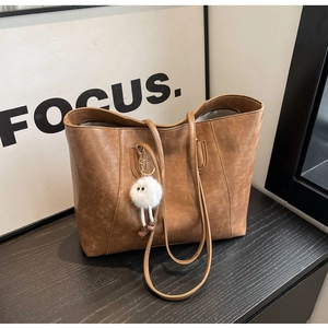 Detailed texture of brown retro faux leather tote bag with fluffy white charm accessory