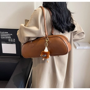 Detail view of brown barrel underarm bag with cute monster charm and leather brand embossing