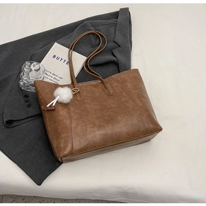 Detail of vintage brown tote bag with leather texture and a white fluffy ball charm