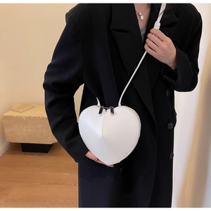 Dettaglio borsa a tracolla bianca a cuore indossata su un blazer nero da una modella