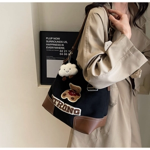 Detail view of black canvas tote bag with brown leather trim and teddy bear embroidery
