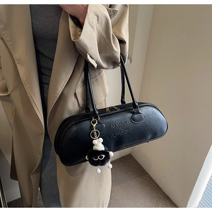 Close-up of black leather cylinder bag with gold zipper and plush charm detail