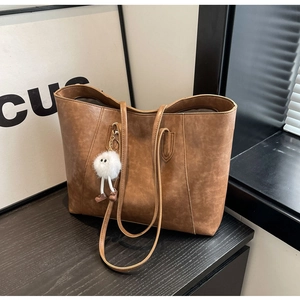 Detail of vintage brown tote bag with leather texture and white plush monster charm accessory