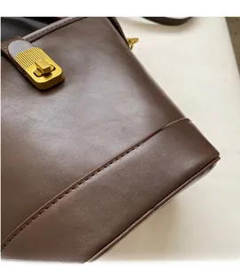 Detail of a brown leather bucket bag showing the golden metal twist lock and stitching