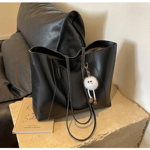 Detail of black faux leather tote bag texture with a cute white plush charm on the strap