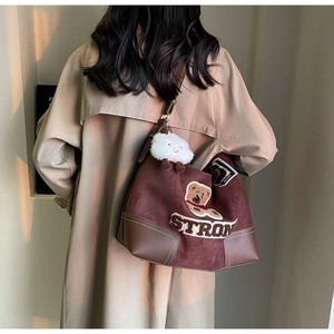 Close-up of brown suede tote bag with bear patch and plush cloud charm in sunset light