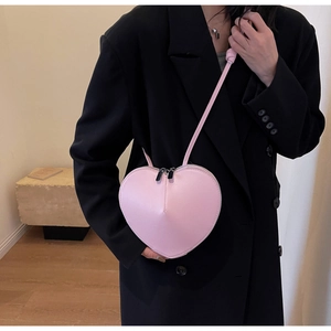 Dettaglio borsa a tracolla rosa a forma di cuore con doppia cerniera indossata su blazer nero