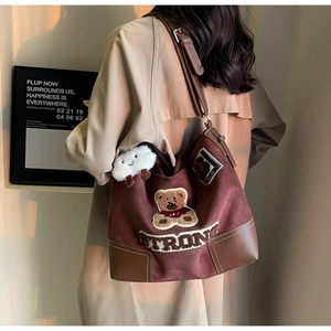 Detail of vintage brown suede tote bag with teddy bear patch and cloud charm on model