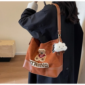 Detail view of caramel brown suede tote bag with teddy bear embroidery and plush charm