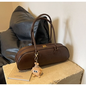 Close-up of dark brown cylindrical shoulder bag with embossed logo and plush charm