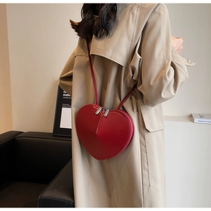 Borsa a tracolla rossa a forma di cuore indossata da una modella in trench beige elegante