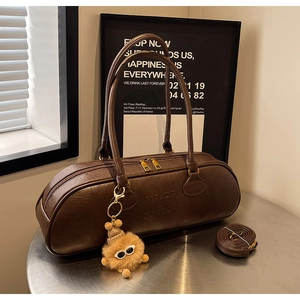 Detail of dark brown leather cylinder bag with gold zippers and plush pendant