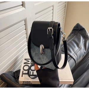Detail of crossbody phone bag showing black leather and blue denim patchwork with buckle