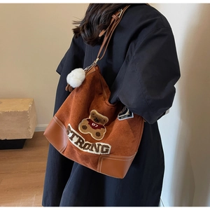 Detail of vintage brown suede tote bag with bear embroidery and white fur ball charm