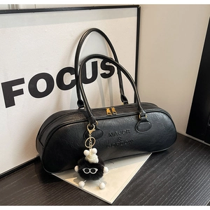 Close-up of black embossed leather cylindrical handbag with gold zippers and plush charm