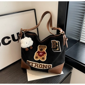 Detail of black canvas tote bag with brown leather trim and fuzzy teddy bear embroidery