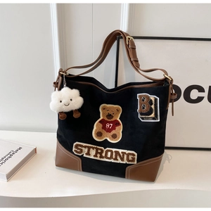 Detail of black canvas tote bag with varsity teddy bear embroidery and brown leather trim