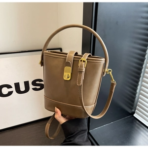 Detail view of brown leather bucket bag showing golden clasp and textured hand strap