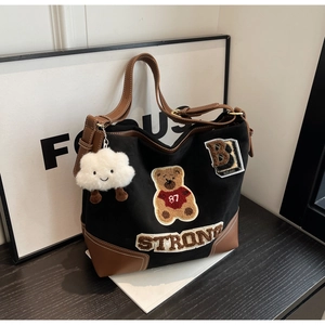 Detail of black canvas tote bag featuring bear embroidery and brown leather patchwork