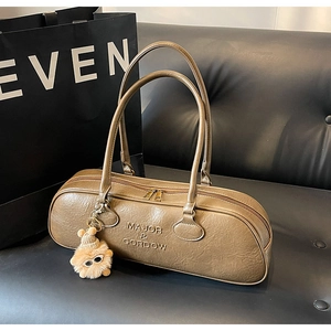 Close-up of a taupe bowling bag with brand embossing and a cute plush sunglasses charm