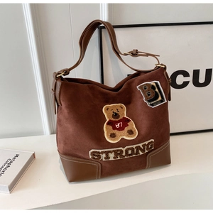 Close-up of brown suede tote bag featuring teddy bear embroidery and adjustable strap