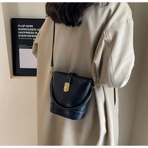 Side view of black bucket bag with gold clasp paired with a beige coat for a chic urban look