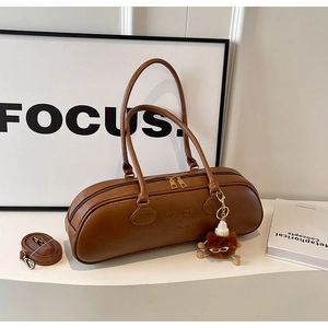 Close-up of brown PU leather barrel bag featuring embossed text and plush bear charm