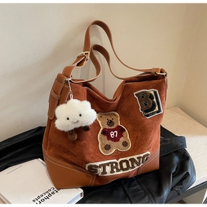 Detail of caramel suede tote bag with retro patches and a white cloud plush charm