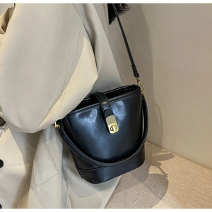 Detail of black bucket bag with gold metal buckle and long strap on a beige coat