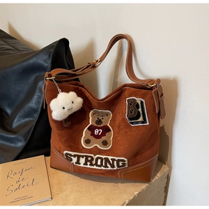 Detail view of brown suede tote bag with retro teddy bear embroidery and fluffy charm
