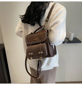 Close-up of vintage brown leather backpack featuring white stitching and gold metal hardware