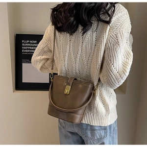 Brown vintage PU leather bucket bag styled with a white sweater in a minimalist indoor setting