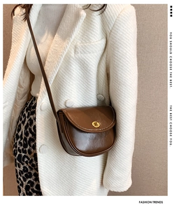 Detailed view of a vintage brown leather saddle bag with a golden circular metal clasp