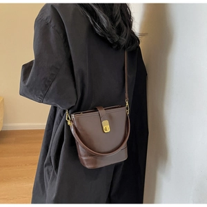Detail view of brown leather bucket bag with gold lock and adjustable strap