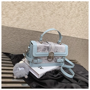Détail du sac en cuir bleu clair avec tissu fleuri, serrure métal et pendentif peluche
