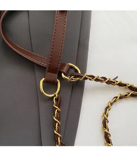 Détail d'une bandoulière en cuir marron avec chaîne en métal doré sur un sac cabas