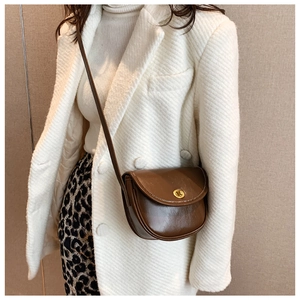 Brown vintage saddle crossbody bag with a golden metallic twist lock on elegant model