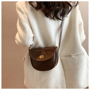 Close-up of a brown vintage saddle bag with gold metal lock on a white tweed blazer