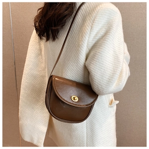 Detail view of a vintage brown saddle bag featuring a circular gold twist lock closure
