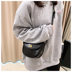 Detail of black leather saddle bag with gold metal clasp on model wearing a grey sweater