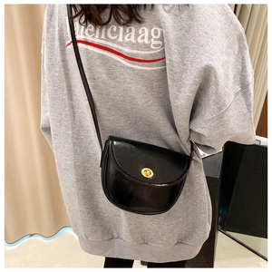 Detail of a black glossy saddle bag featuring a gold oval twist lock and a slim leather strap