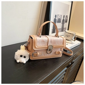 Détail d'un sac bandoulière beige avec texture florale et pendentif en peluche