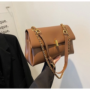 Détail du sac cabas en cuir caramel avec boucle dorée et bandoulière sur un blazer