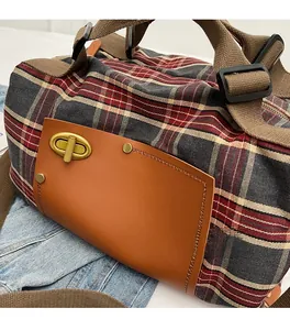 Detail of red and grey plaid travel bag featuring brown leather trim and gold metal buckle