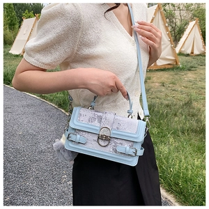 Détail du sac bandoulière bleu clair avec tissu texturé, fermoir métal et pompon