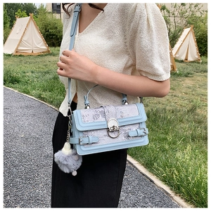 Détail d'un sac à main bleu clair en cuir avec tissu gris et pendentif pompon