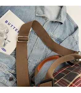 Detail view of plaid bag featuring adjustable brown canvas strap and vintage metal buckle